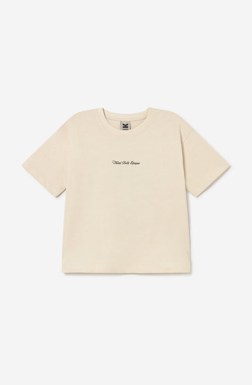 Camiseta relaxed fit de algodón orgánico color ivory con logo Hotel Belle Époque en el pecho y gran ilustración vintage de un botones con perros y equipaje en la espalda.