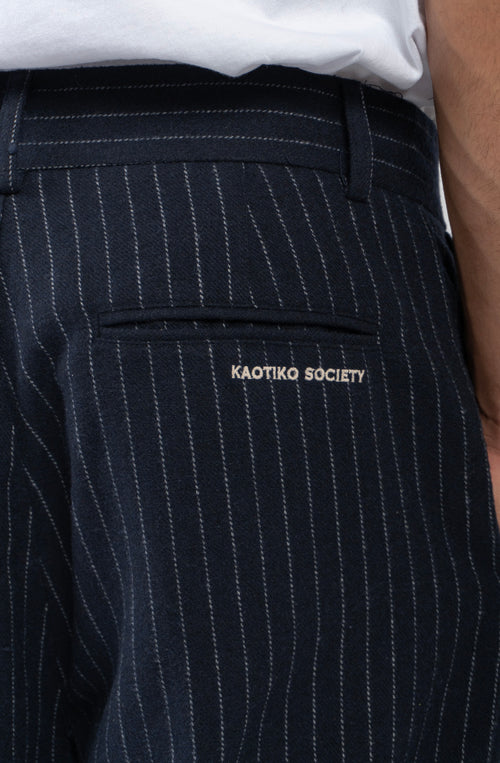 Pantalón Belle Époque navy de raya diplomática blanca con pinzas delanteras, pernera ancha y detalle Kaotiko Society trasero.