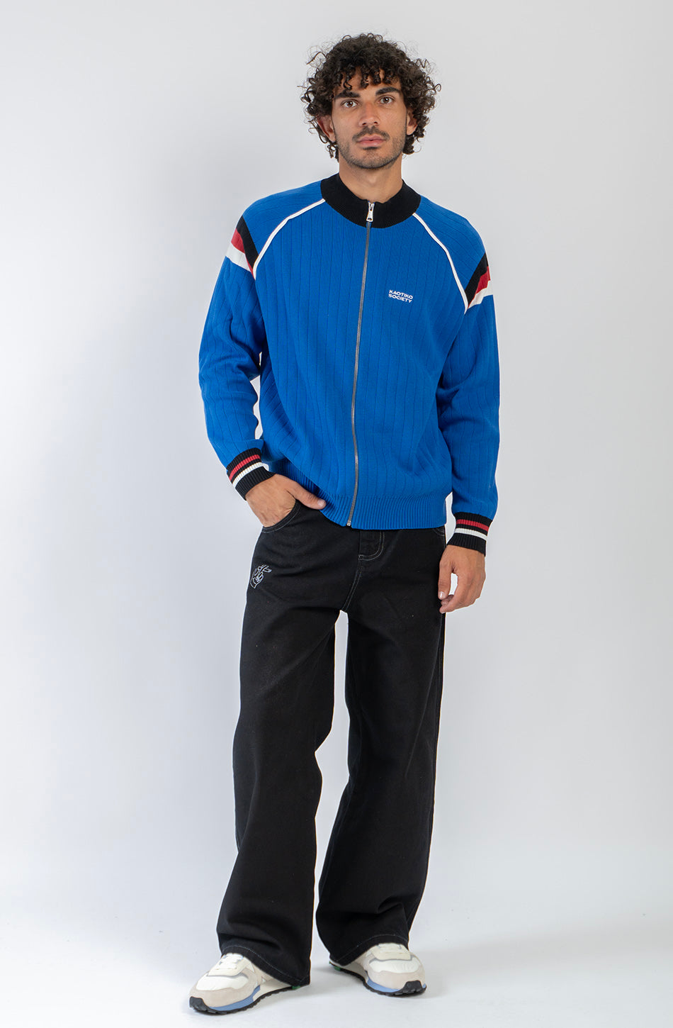 Chaqueta de punto azul con cremallera, cuello bomber y detalles deportivos en blanco, negro y rojo.