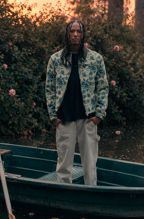Chaqueta unisex de tejido tapestry con estampado floral en tonos verde, azul y crema, cuello de pana en contraste, cierre de cremallera y bolsillo de pecho con cremallera.