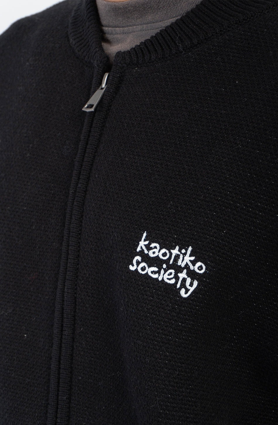 Jersey unisex de punto negro con cremallera, bordado Kaotiko Society en el pecho y gráfico jacquard de flores azules con mensaje Bad Romance en la espalda.