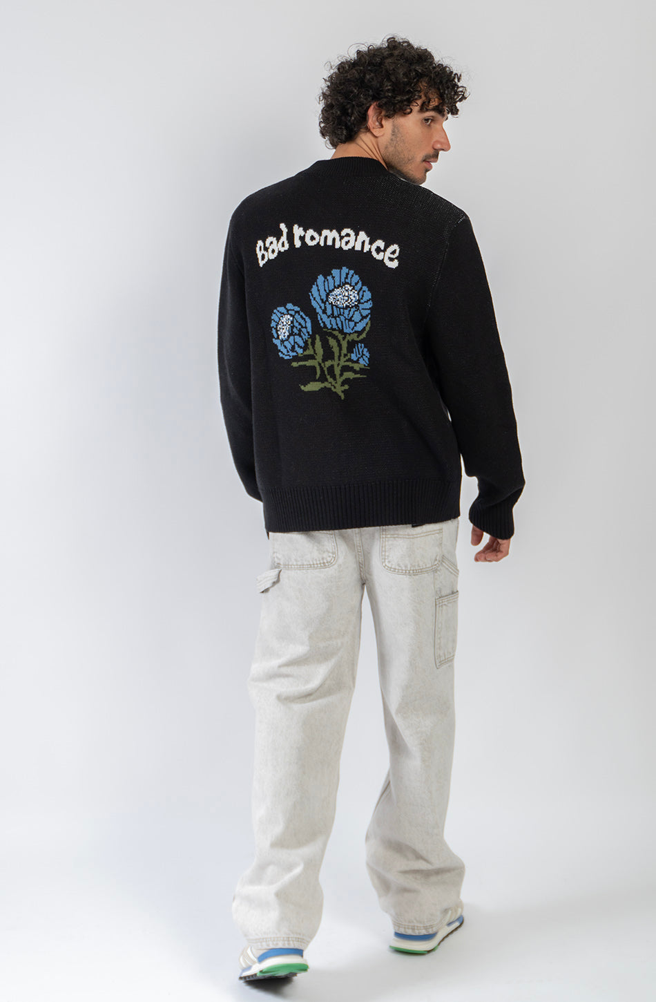 Jersey unisex de punto negro con cremallera, bordado Kaotiko Society en el pecho y gráfico jacquard de flores azules con mensaje Bad Romance en la espalda.