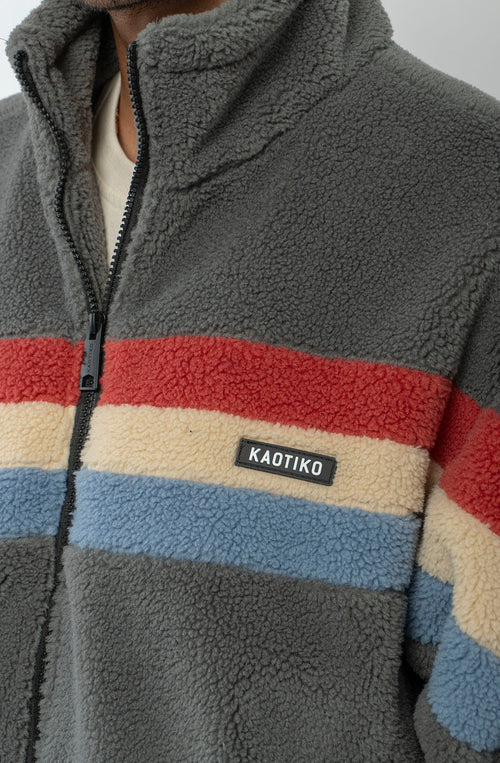 Polar Wabi Sabi Khaki de fleece con franjas rojas, beige y azules, cuello alto y cierre de cremallera.